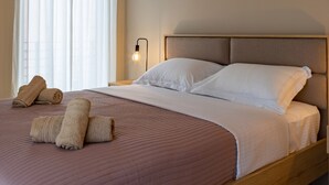 Ein ordentlich gemachtes Bett mit einer rosa Steudecke, weißen Kissen und aufgerollten Handtüchern an der Seite.