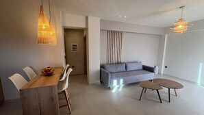Uma sala de estar moderna com uma mesa de jantar de madeira, cadeiras brancas, um sofá cinzento e uma mesa de centro redonda.