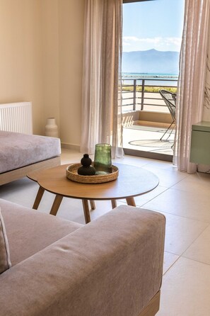 A modern hotel room with a sofa, a small round table with a decorative item, a view of the sea and mountains through a balcony. - ΟliveVine2 · OliveVine2-Πολυτελές Διαμέρισμα με Θέα Ναύπλιο (Nafplio)