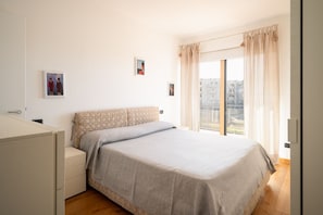 Un dormitorio con cama, mesita de noche, armario y ventana con cortinas.