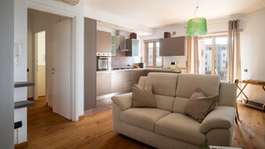 A modern living room with a beige sofa, a kitchen in the background, and a green pendant light. - Gimber Lofts 2 by Klodge- vintage flat with Wi-Fi (Olbia)