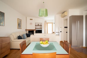 Una sala de estar con un sofá, una mesa de comedor con sillas, una chimenea y una zona de cocina con un refrigerador.