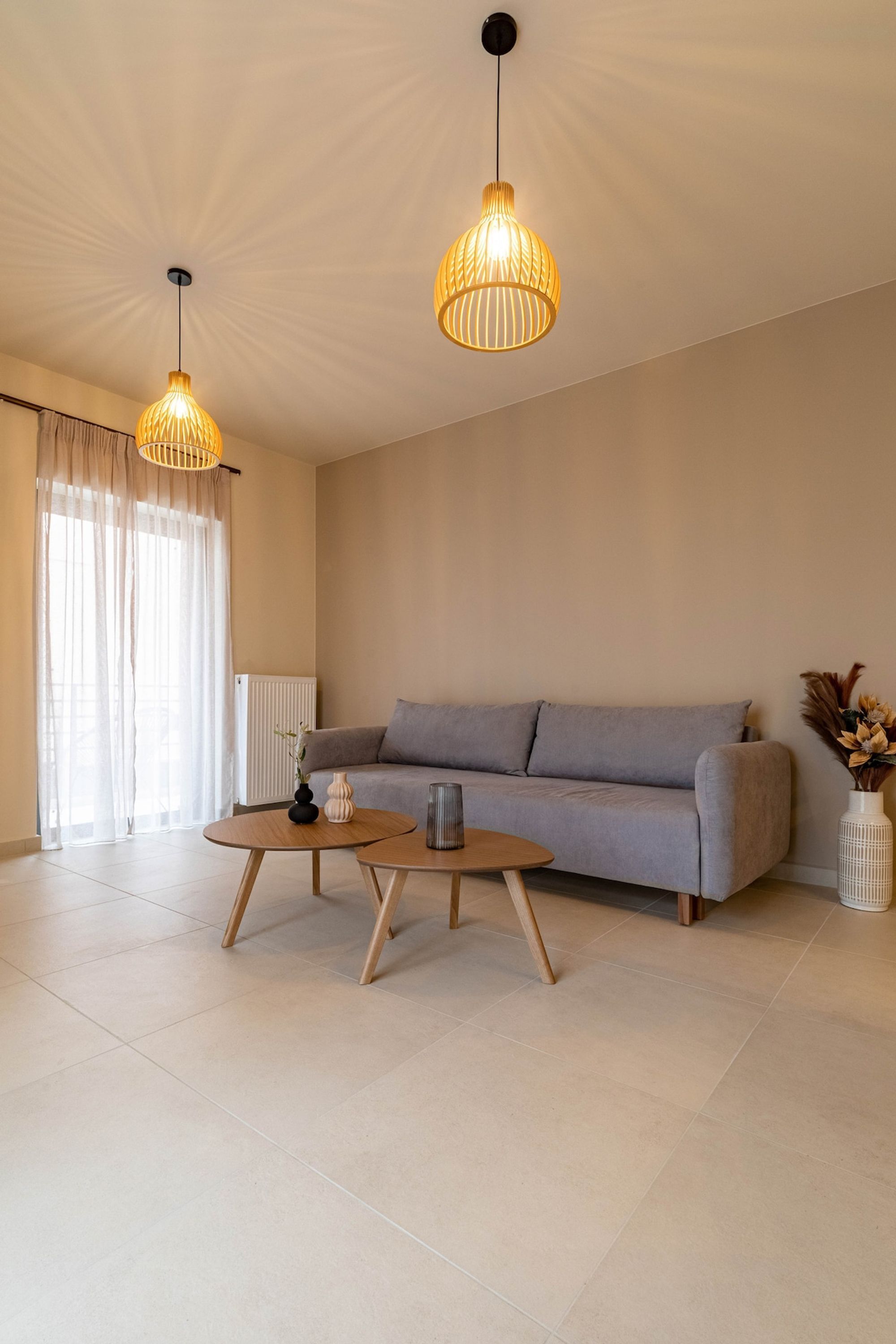 A modern living room with a grey sofa, two wooden coffee tables, and two hanging pendant lights.