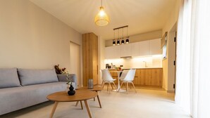 Een moderne woonkamer met een bank, een salontafel, en een eethoek met stoelen, met een keuken op de achtergrond.