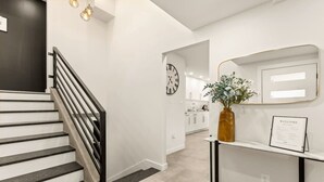 Een modern interieur met een trap, een wandklok, een welkom bord en een vaas met bloemen.