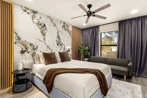 Ein modernes Schlafzimmer mit einem Bett, einer Couch, einem Deckenventilator und einem großen Fenster mit Vorhängen.