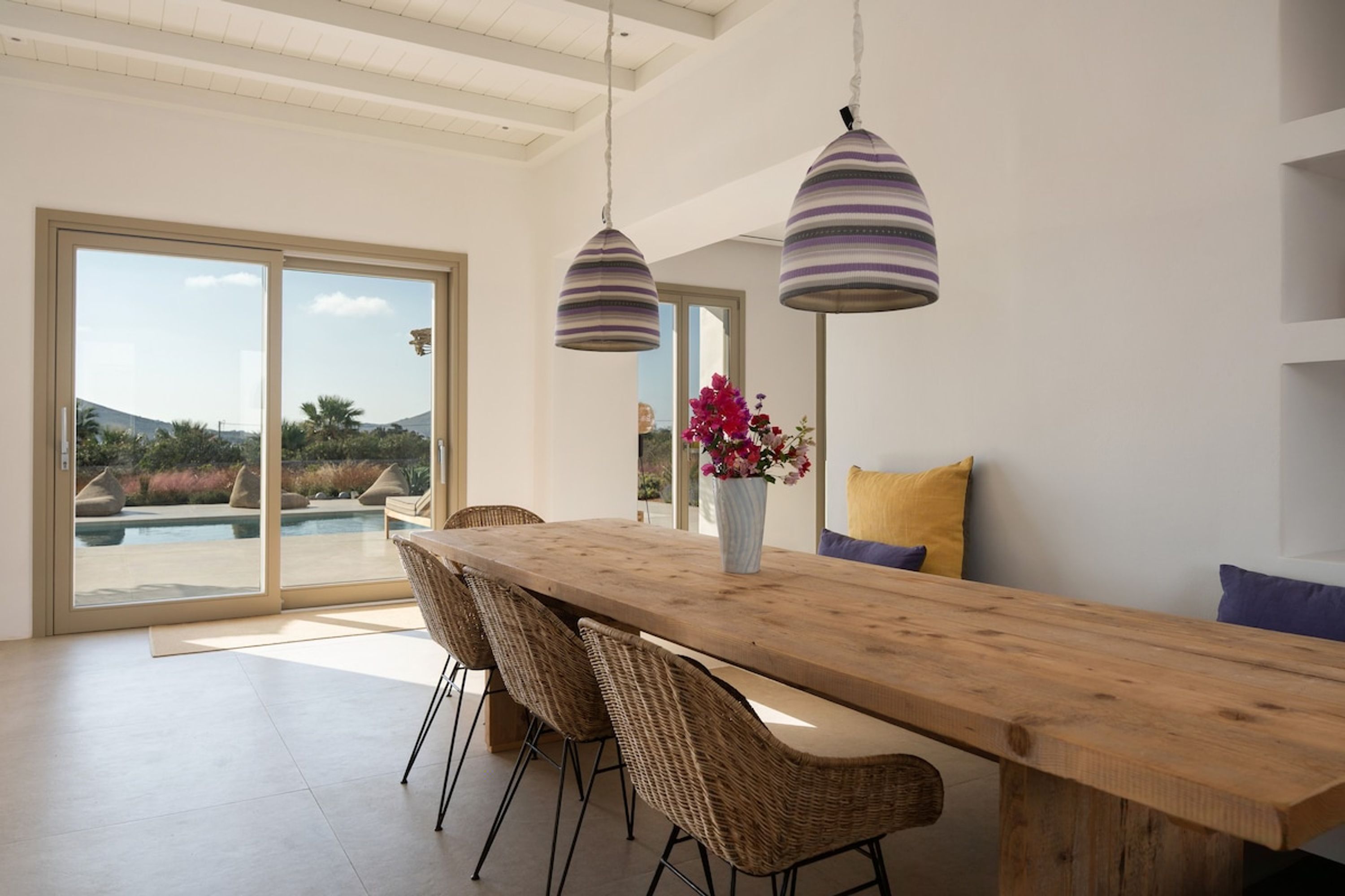 Un espace de repas moderne avec une table en bois, des chaises en osier et des suspensions à motifs rayés.