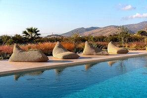 Un espace aménagé au bord de la piscine, avec quatre poufs tressés et une vue dégagée sur les montagnes en arrière-plan.