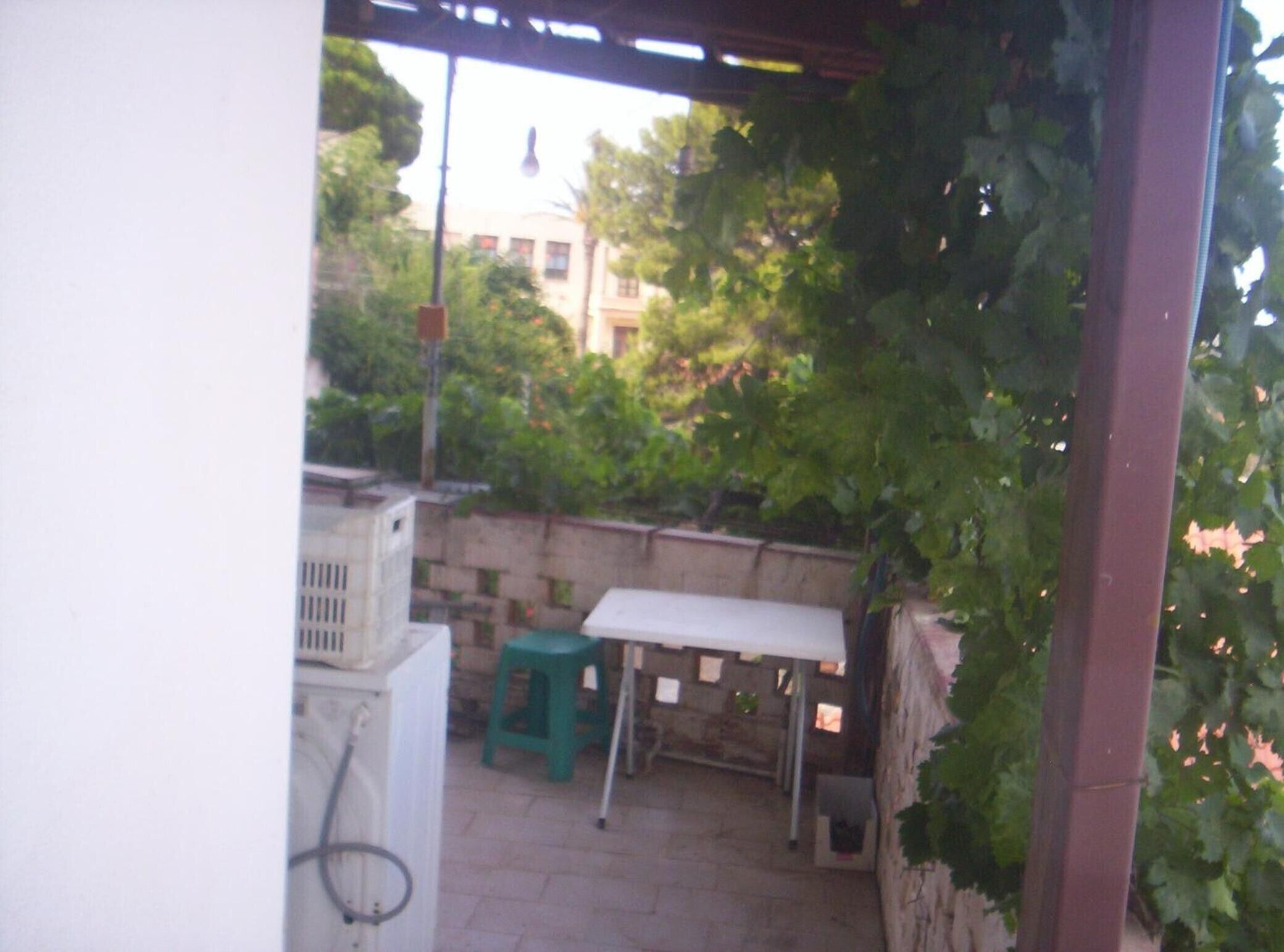 Un'area patio con un tavolo e uno sgabello verde, circondata da un muro in pietra e vegetazione.