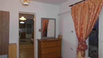 A room with a wooden dresser, a mirror, a chandelier, and a door leading to a kitchen.