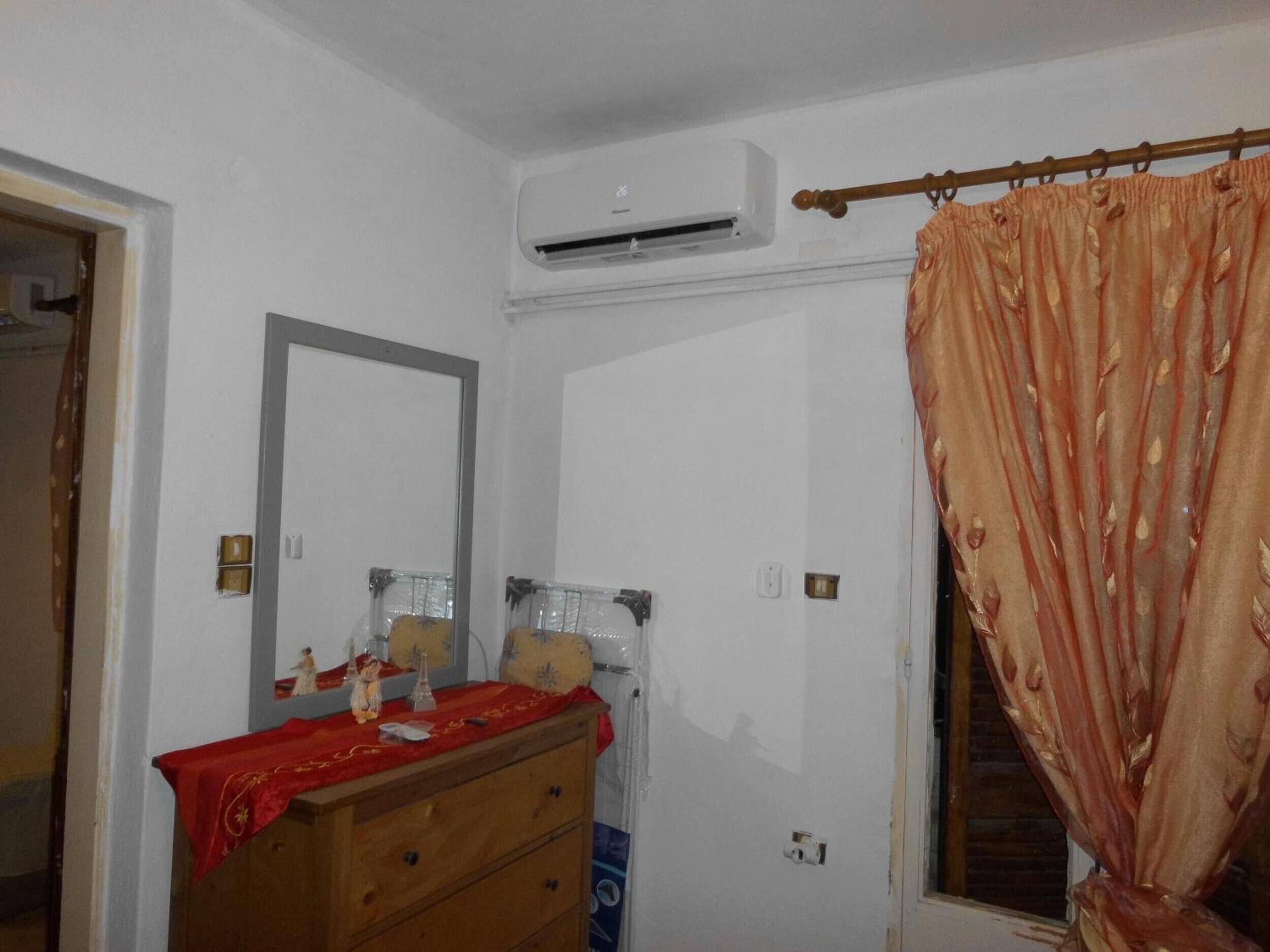 Una habitación con un aparador de madera, un espejo, un equipo de aire acondicionado y una ventana con cortina.