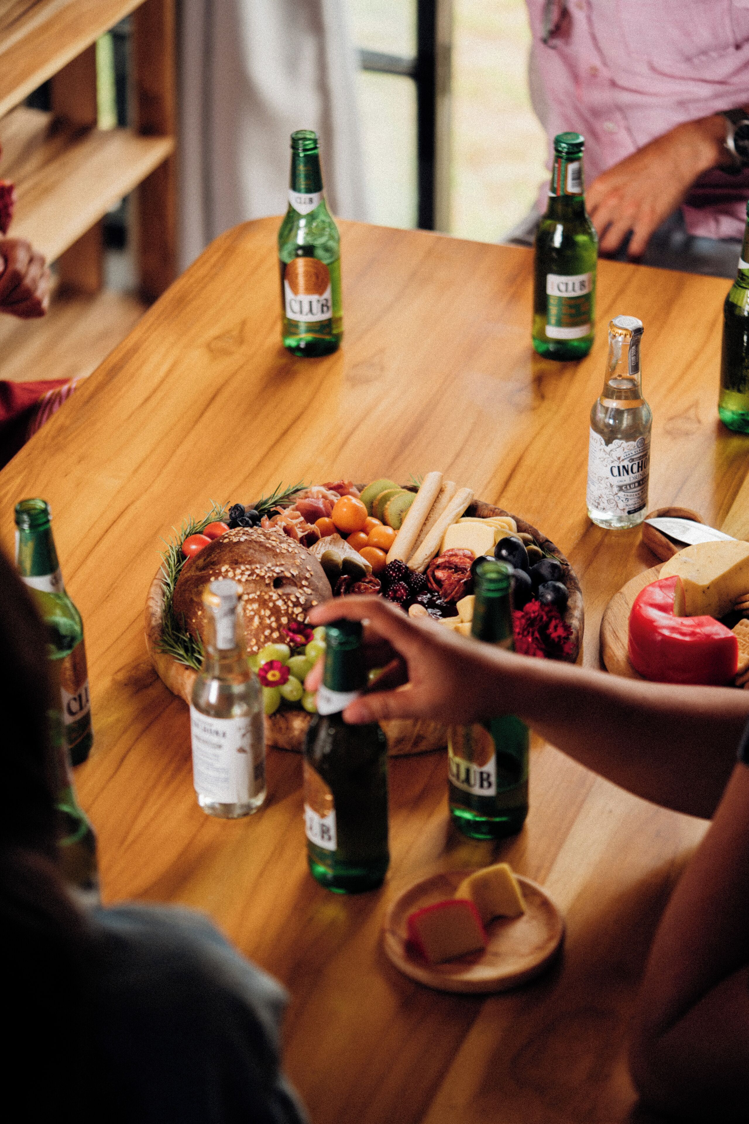 A wooden table with a variety of food items and bottles, likely for a gathering or party.