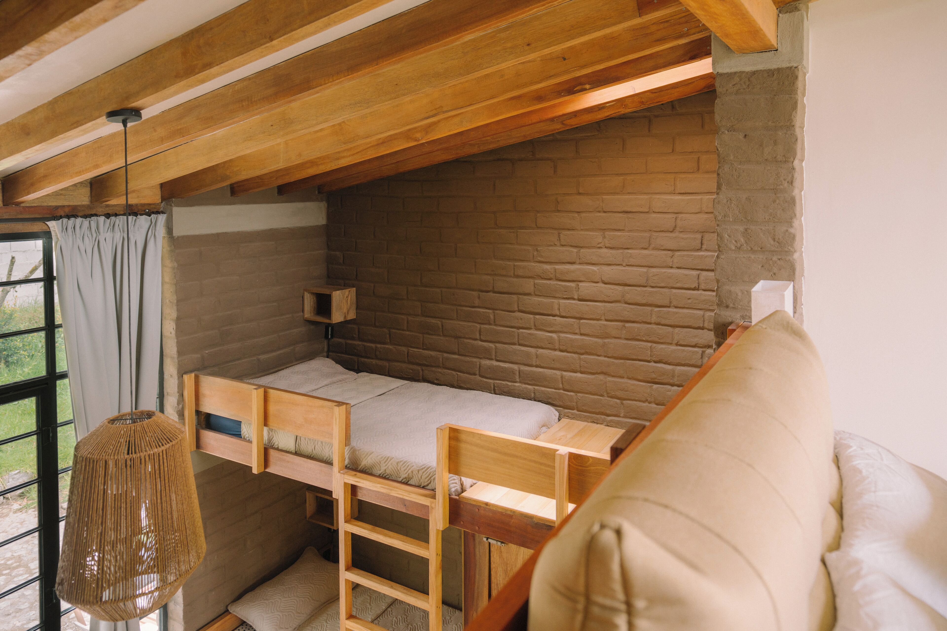 Una habitación acogedora con una cama nido de madera, una lámpara colgante y vistas al exterior a través de una ventana.
