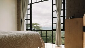 Ein Schlafzimmer mit großem Fenster, einem Bett mit gemustertem Überwurf und einer Holzkommode.