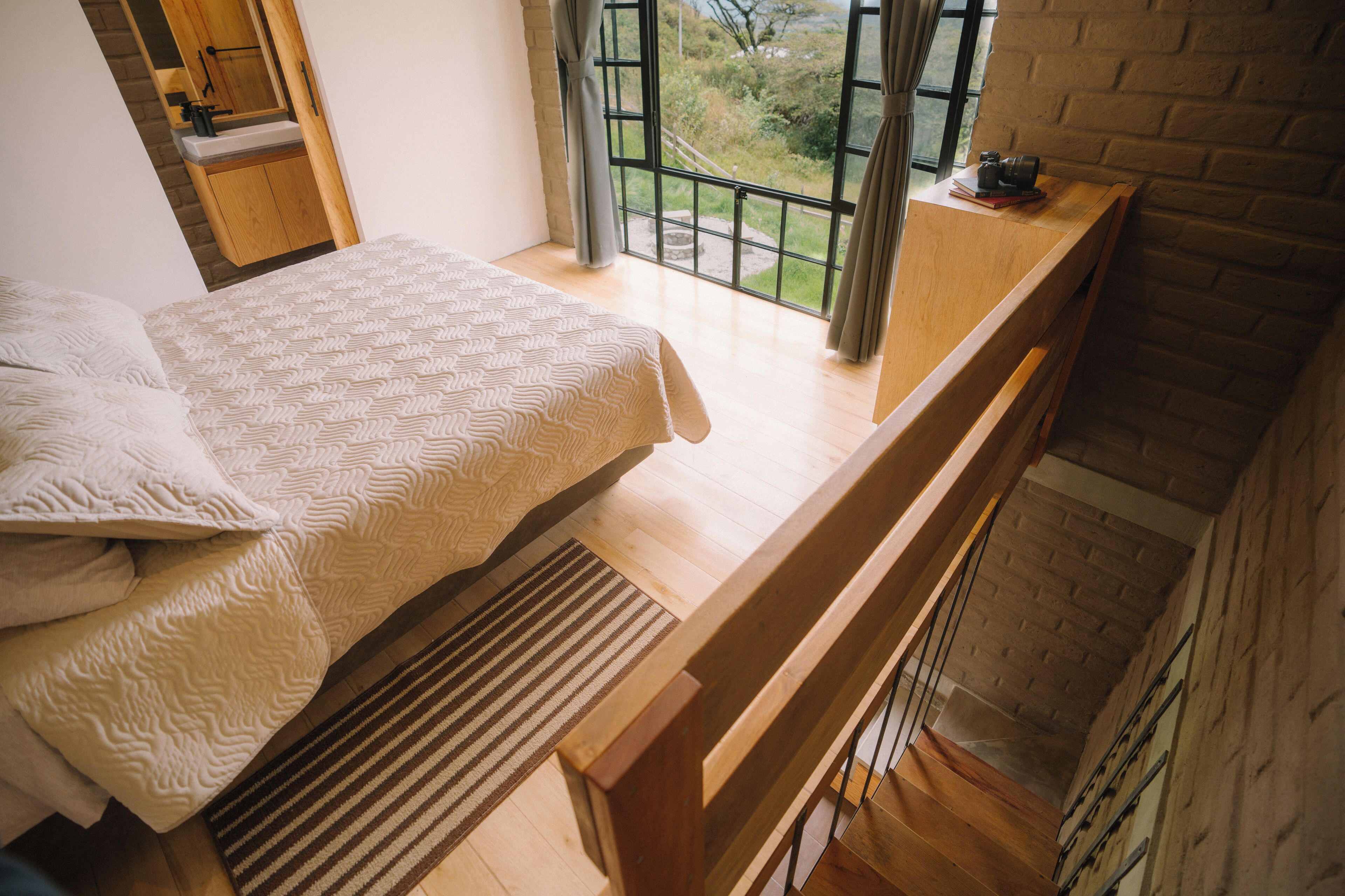 Een slaapkamer met een bed, een houten bankje, een raam met uitzicht en een tafeltje met een camera.