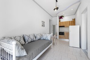 A modern living room with a sofa, a dining table, and a kitchen area with wooden cabinets and a refrigerator. - Sun & Beach Apartment in Chania 8 (Chania)