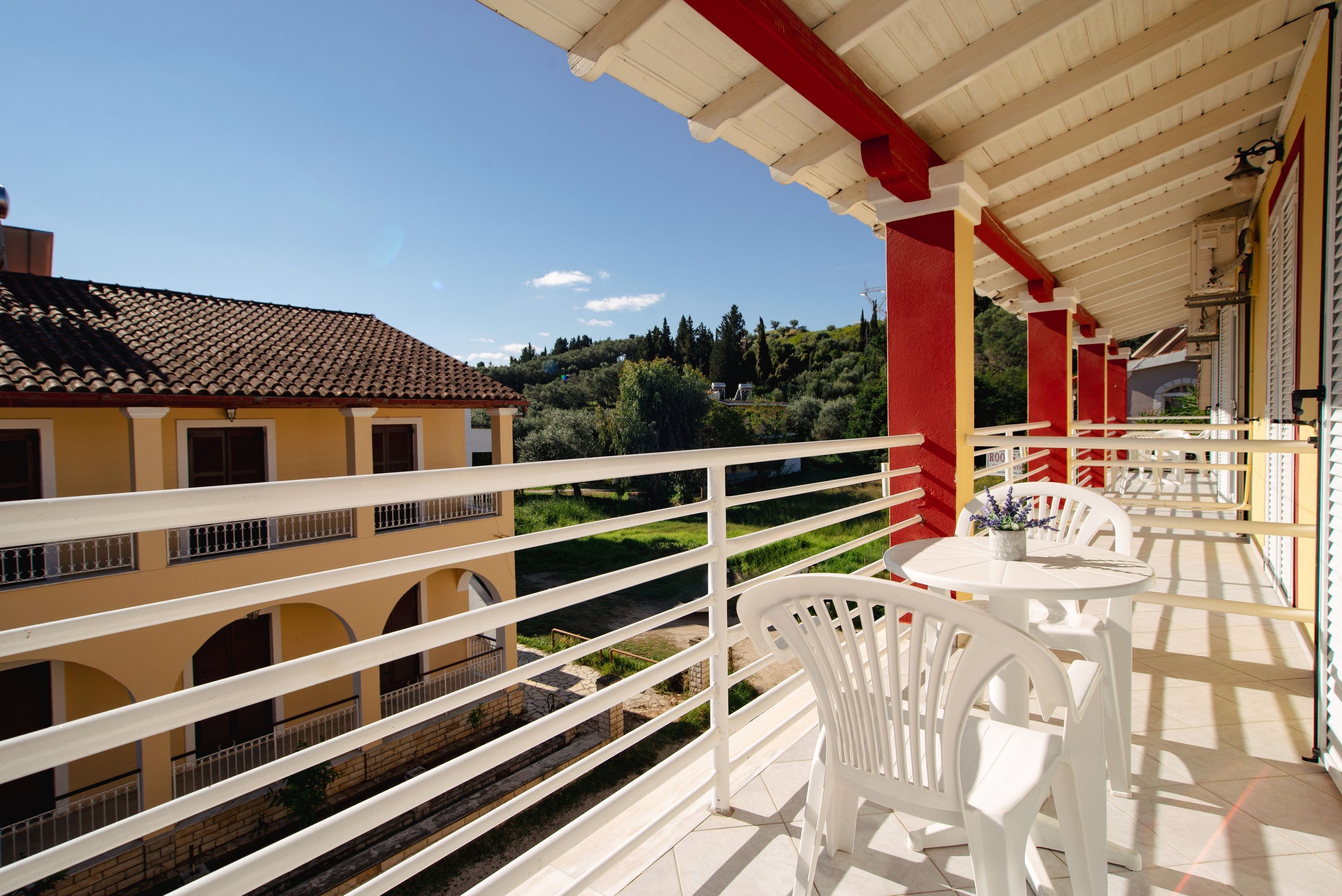 Ein Balkon mit weißen Stühlen und einem Tisch, mit Blick auf einen Garten und Gebäude.