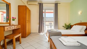 Quarto de hotel com uma escrivaninha de madeira, duas camas, um espelho grande e vista para um edifício pela janela.