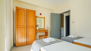 Una habitació d'hotel amb dos llits, un armari de fusta, una taula petita amb un ram de flors i un mirall sobre la tauleta de nit.