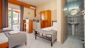 Hotellihuone, jossa on kaksi sänkyä, pieni keittiönurkkaus, kylpyhuone, jossa on pesuallas ja peili, sekä näkymä ulos.