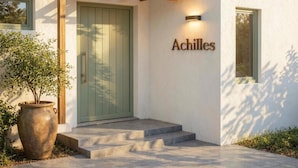 Una entrada de edificio moderna con una puerta verde, una placa con el nombre "Achilles" y una estructura de pérgola sobre la puerta.