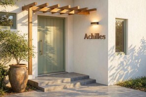 Ein moderner Gebäudeeingang mit einer grünen Tür, einer Namensschild mit der Aufschrift „Achilles“ und einer Pergola über der Tür.