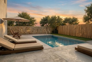 A swimming pool with lounge chairs and an umbrella, surrounded by a stone wall and a wooden fence. - Villa Michael with Swimming pool (Agriana)