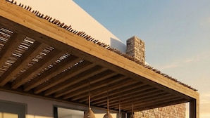 Een buiten eethoek met een houten pergola, een stenen muur en hangende rieten lampen.