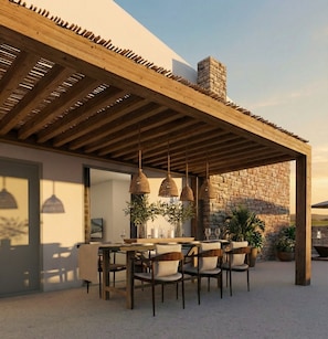 Ein Essbereich im Freien mit einer Holz-Pergola, einer Steinmauer und hängenden Korblampen.