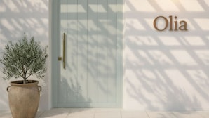 Een lichtblauwe deur met een messing handgreep, een bloempot links en de naam "Olia" rechts op de muur.