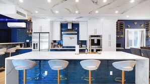 Een moderne keuken met een marmeren aanrechtblad, barstoelen en een blauwe betegelde achterwand.
