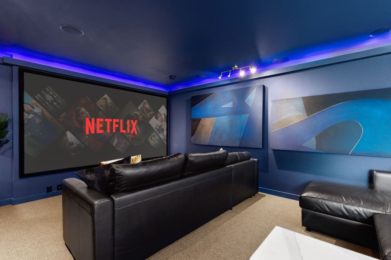 A home theater room with a large screen displaying 'NETFLIX', a black leather couch, and abstract wall art.