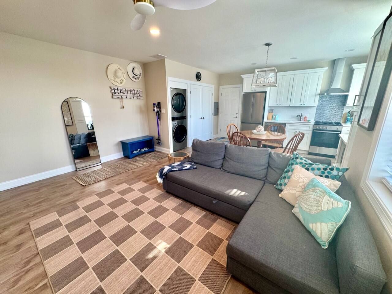 A living room with a sofa, a rug, a dining area, and a kitchen in the background.