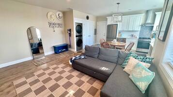 A living room with a sofa, a rug, a dining area, and a kitchen in the background.