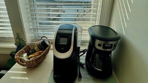 Eine Küchenarbeitsfläche mit Kaffeemaschine, Wasserkocher und einer Korb voller Gegenstände.