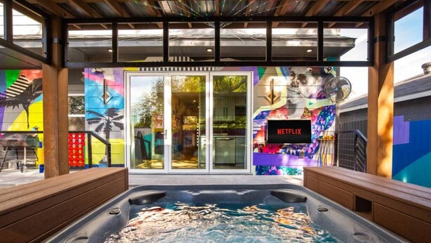 A hot tub area with a Netflix sign, colorful murals, and a wooden deck. - City Views Rooftop Karaoke, Pool, Hot Tub, Games (San Antonio)