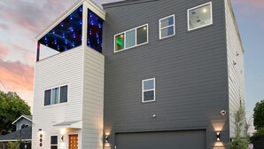 A modern two-story house with a garage, a covered patio, and a small garden area. - City Views Rooftop Karaoke, Pool, Hot Tub, Games (San Antonio)