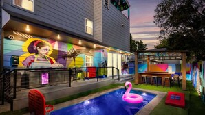 A pool area with a flamingo float, a basketball hoop, and a mural on the building. - City Views Rooftop Karaoke, Pool, Hot Tub, Games (San Antonio)