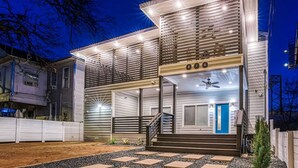 A modern two-story house with a covered front porch, a visible staircase, and a blue door. - Stylish 6BR/5BA, DT, Hot Tub, Games, Sleeps 20+ (San Antonio)