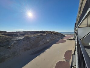 A beach view from a balcony with a clear sky and sun.