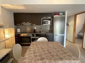 A compact kitchen with a microwave, stove, and refrigerator. There is a dining table with chairs. - Cozy Seaside Apartment with Pool and Private Parking in Roses (Roses)