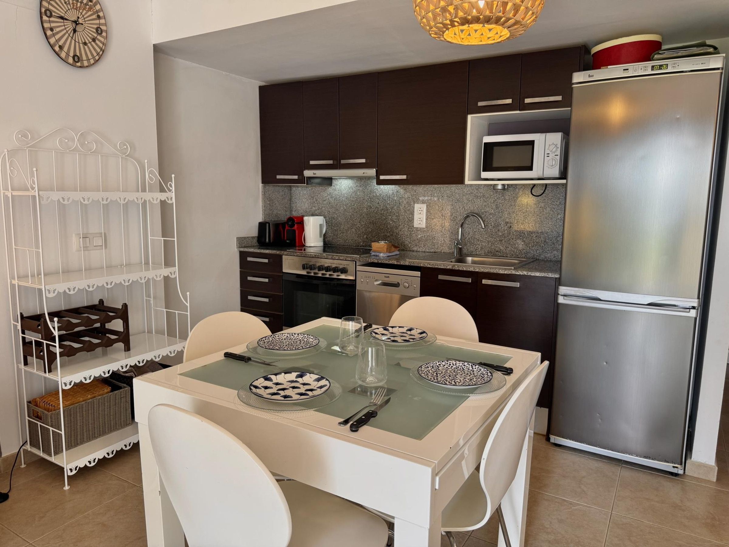 A compact kitchen with dark cabinets, a stainless steel refrigerator, a microwave, and a dining table with chairs.