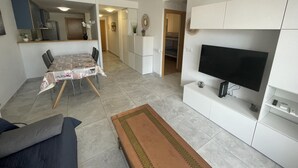 Een functionele leefruimte met een eethoek, kitchenette en een aan een kast bevestigde televisie.
