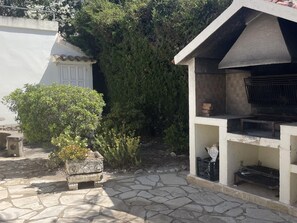 Kivipäällysteinen terassi, jossa on grilli ja pieni puutarha-alue.