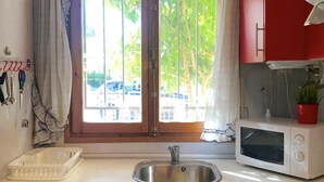 A kitchen with a stainless steel sink, a microwave, and a window with curtains. - Charming Family House Near Beach with Pool (Miami Playa)