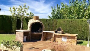 A brick outdoor kitchen with a chimney, surrounded by well-maintained hedges and flower beds. - Charming Family House Near Beach with Pool (Miami Playa)