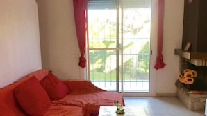 A living room with a red sofa, a small table with a plant, and a view of greenery through a sliding glass door. - Charming Family House Near Beach with Pool (Miami Playa)