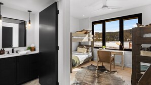Un dormitorio moderno con una cama litera, un escritorio y un amplio ventanal con vistas al bosque.