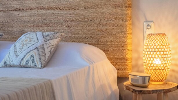 A bed with a patterned pillow, a textured wall, and a table with a lamp. - Charming apartment in La Fosca - 4 guests (Palamós)