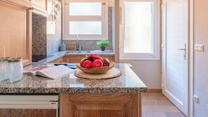 A kitchen with granite countertops, wooden cabinets, a bowl of fruit, and a window with frosted glass. - Charming apartment in La Fosca - 4 guests (Palamós)